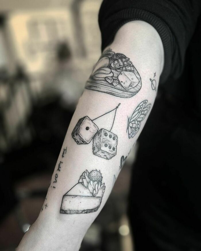 Forearm with patchwork tattoos, featuring dice and food designs in black ink.