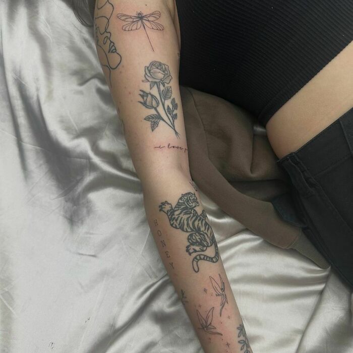 Arm showcasing patchwork tattoos, including a tiger, rose, and dragonfly, on a person lying on a bed.