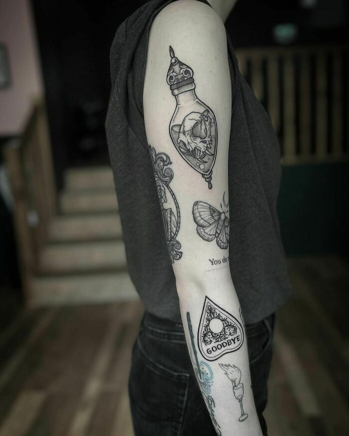 Detailed patchwork tattoos on a person's arm featuring a bottle, butterfly, and Ouija planchette.