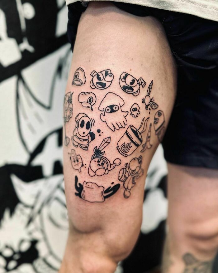 Cartoon-themed patchwork tattoo on thigh with various playful characters and objects.
