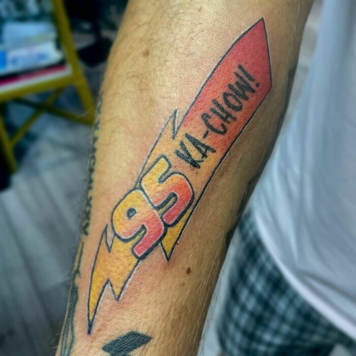 Pop culture tattoo featuring "95 KA-CHOW!" in vibrant colors on a person's forearm.