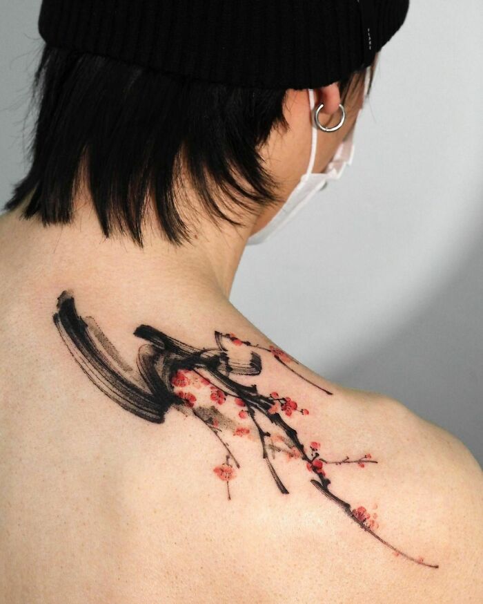 Person with a tree tattoo on their back, featuring black and red ink.