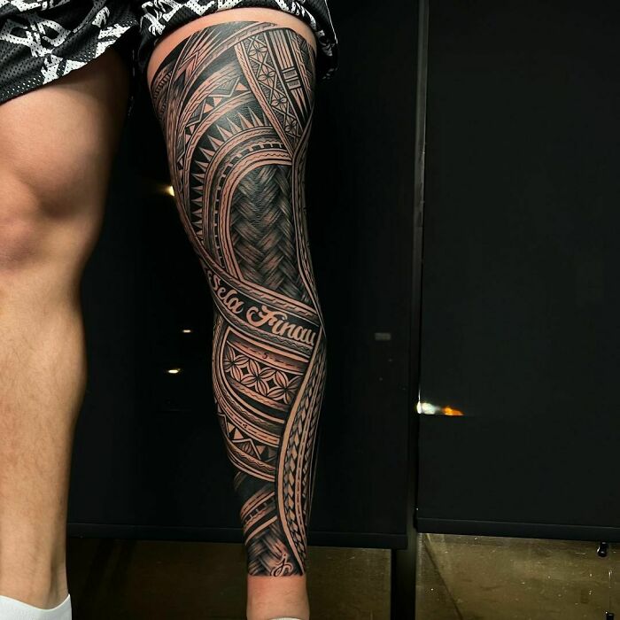 Intricate tribal tattoo design on a person's leg, showcasing detailed patterns and lettering.