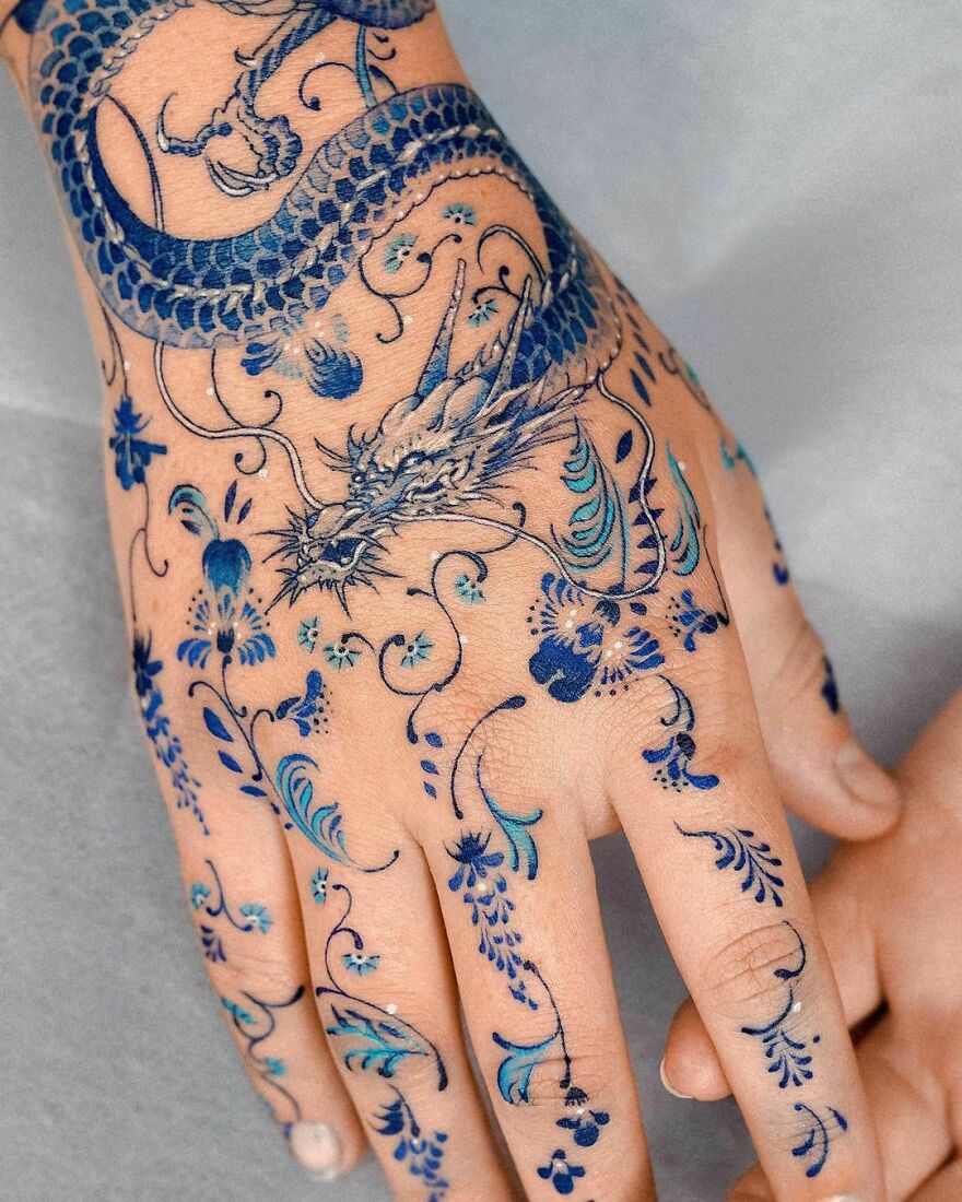 Blue dragon tattoo on hand with intricate floral designs.