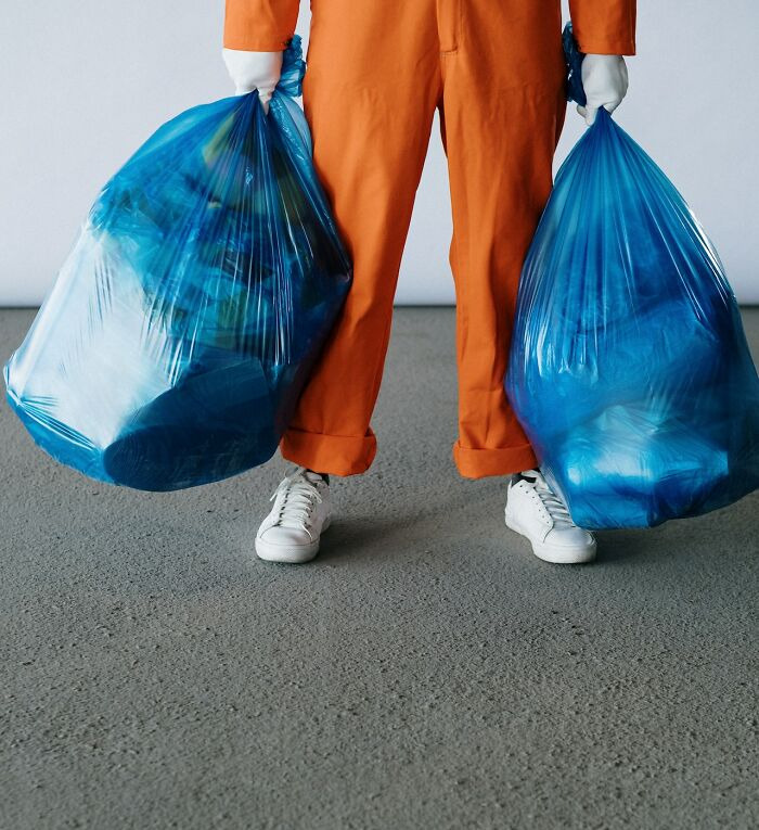 Person in orange outfit holding two large blue garbage bags, illustrating things not to buy cheap shared in an online community.