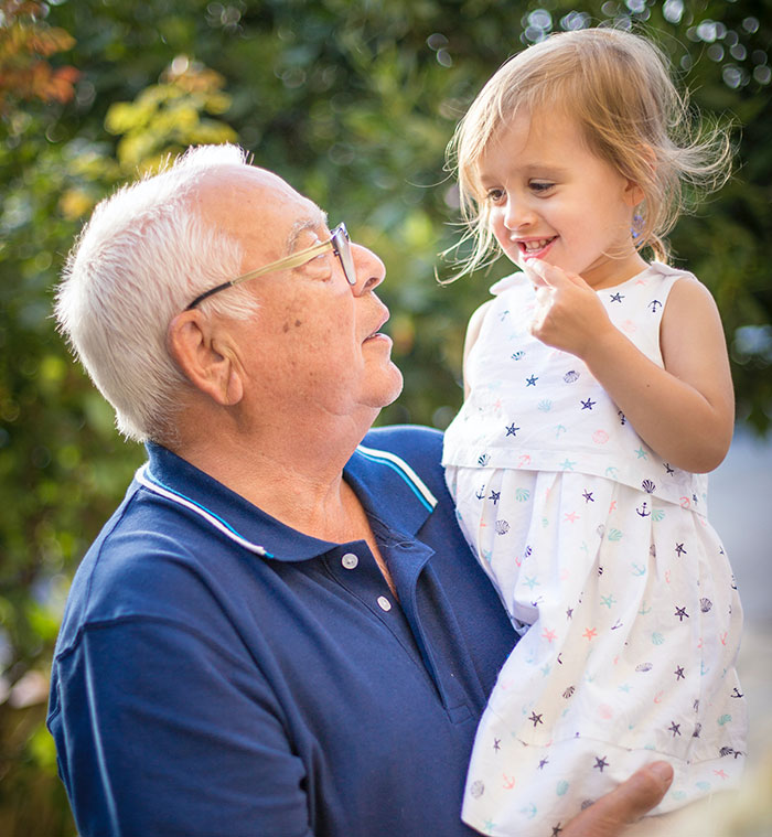 Grandpa smiling and holding his granddaughter outdoors, sharing loving moments and wise advice from grandparents.
