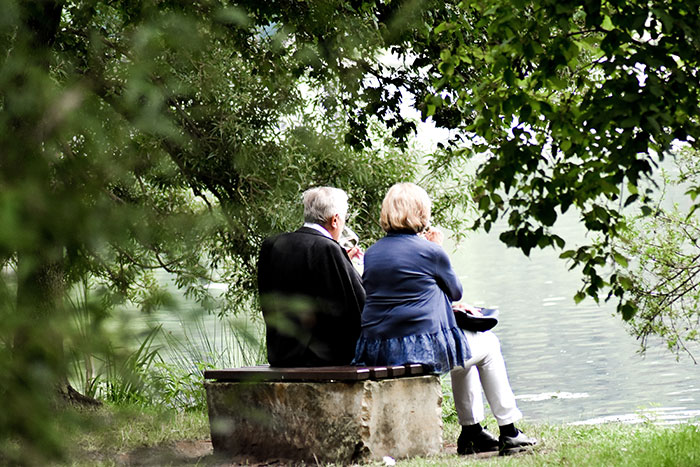Grandparents sitting by a calm lake, enjoying a peaceful moment surrounded by lush greenery and nature.