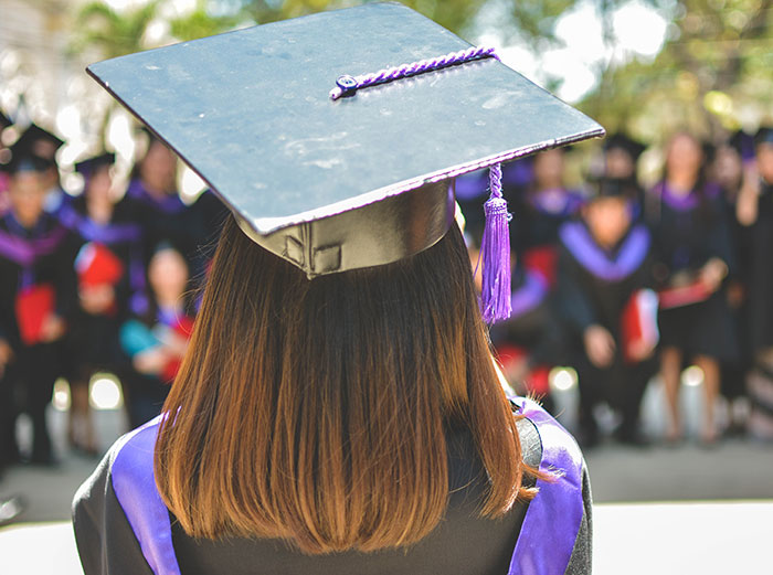 Woman in graduation clothes standing outdoors with a group, symbolizing wise funny and naughty advice from grandparents.