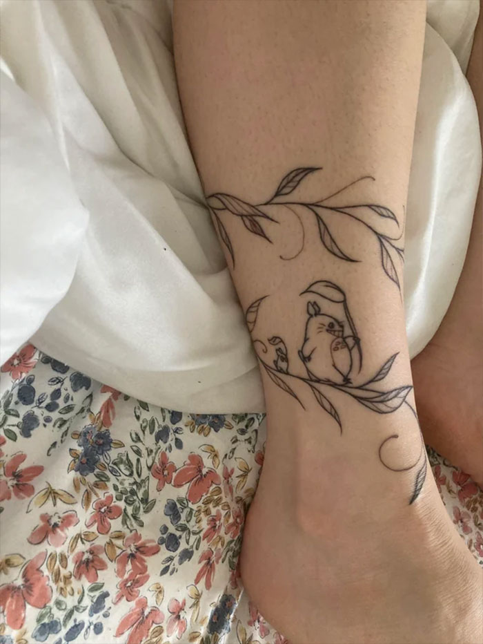 Ankle tattoo of Totoro and leaves on a person's leg, showcasing a minimalist design for tattoo care inspiration.