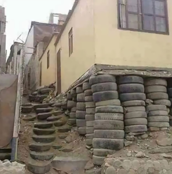 Cursed meme of a building supported by stacks of tires, creating an unusual appearance.