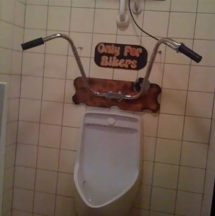 Cursed bathroom urinal with bike handlebars and a sign saying "Only for Bikers."