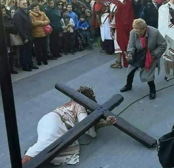 Cursed meme depicting Jesus carrying a cross while a crowd watches, with a woman taking a photo.