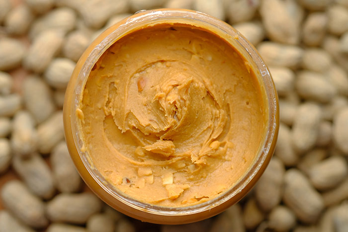An open jar of peanut butter surrounded by peanuts, revealing food history facts about this popular spread and what we eat.