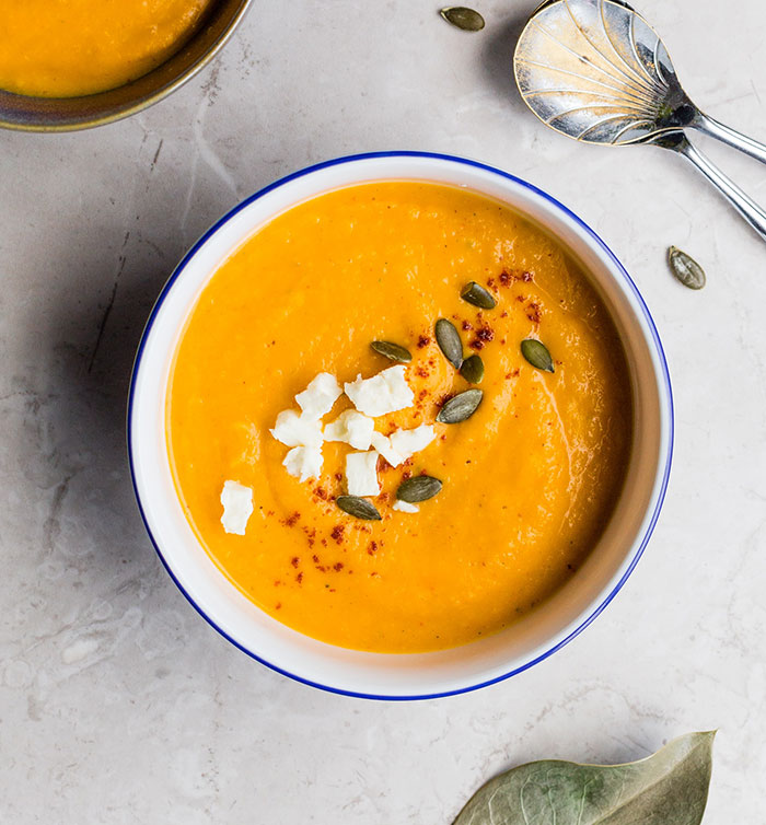 A bowl of delicious orange soup with feta and pumpkin seeds, offering food history facts about what we eat.