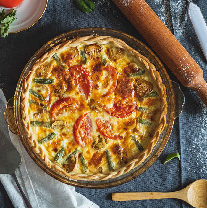 A freshly baked quiche with tomatoes and asparagus, showcasing the flavorful food history of savory pies.