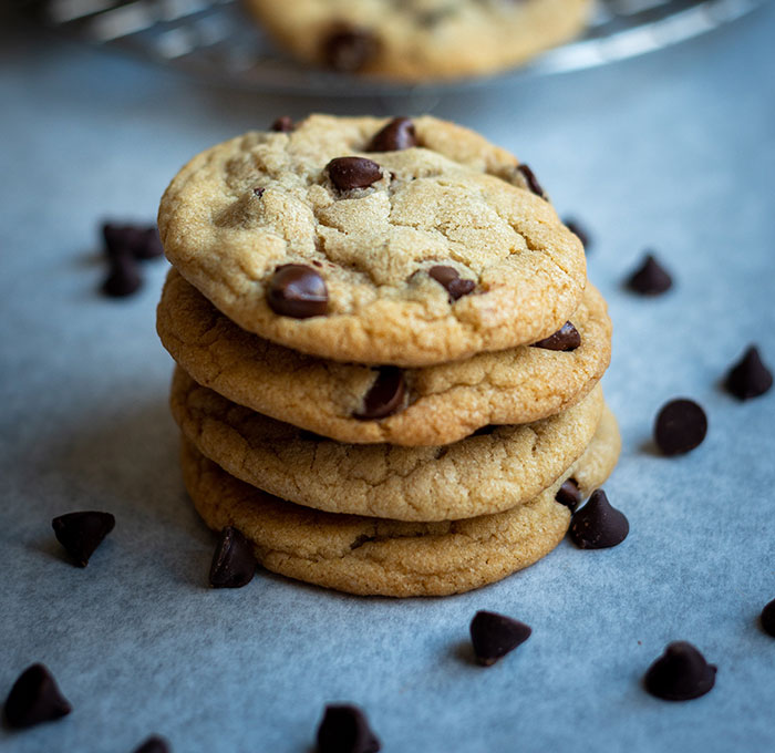 A stack of four chocolate chip cookies on parchment paper, surrounded by loose chocolate chips, demonstrating food history facts.