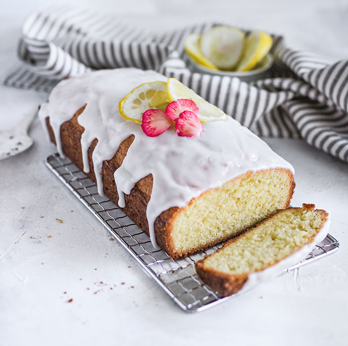 A freshly baked lemon loaf cake with white glaze and lemon slices, cooling on a wire rack, revealing food history facts.