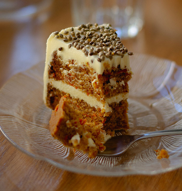 A slice of carrot cake with white frosting and seeds on top, with a bite taken out, illustrating food history facts.