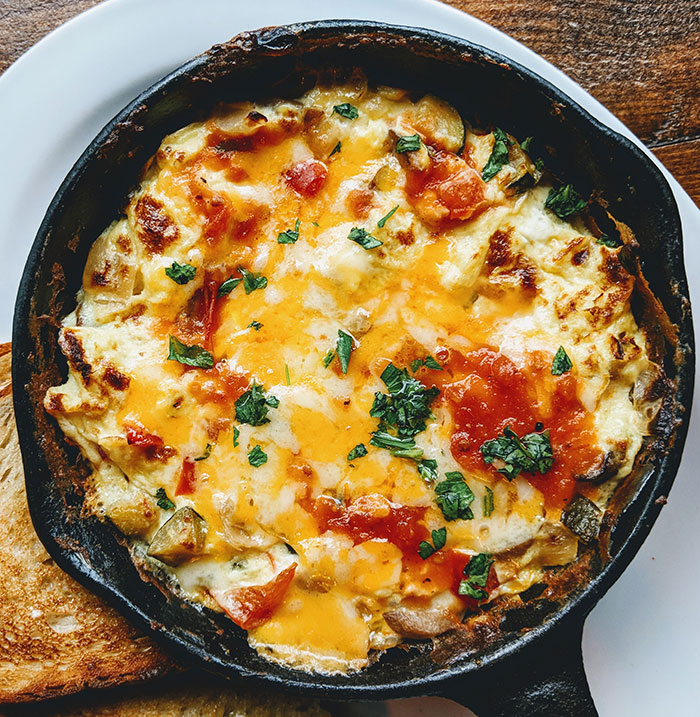 A sizzling skillet of eggs with melted cheese and herbs, a delicious example of food history and culinary evolution.