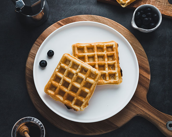 Food history facts: Two waffles on a white plate with blueberries and syrup, emphasizing the story behind what we eat.