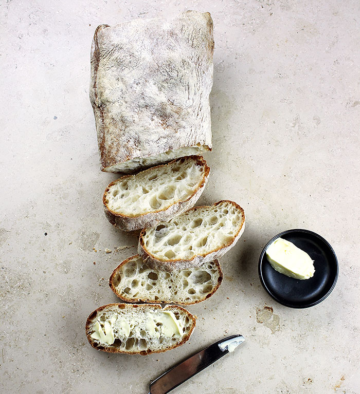 A freshly baked loaf of bread, sliced and buttered, next to a small dish of butter, highlighting food history.