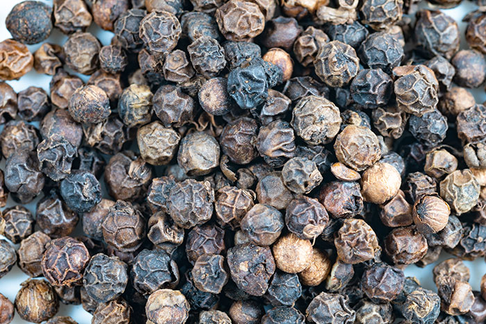 A close-up of whole black peppercorns, highlighting food history facts.