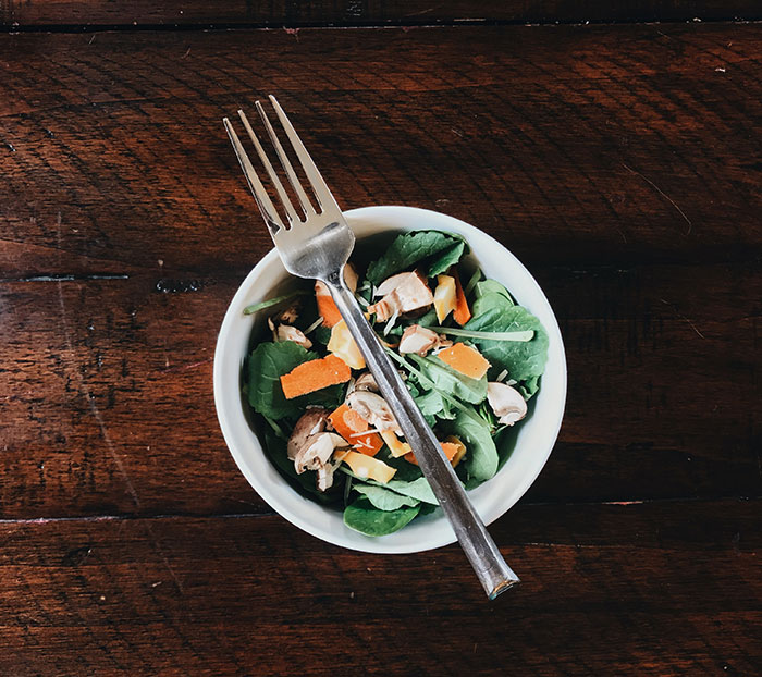 A small bowl of fresh salad with a fork on a wooden table, showcasing food history facts.