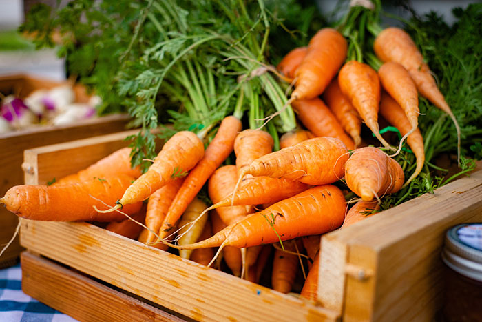 Food history facts: Fresh carrots with green tops in a wooden crate at a market, showcasing the story behind what we eat.