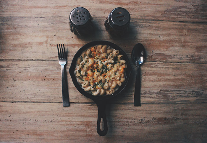 Mac and cheese in a cast iron pan with a fork, spoon, and shakers, highlighting food history.