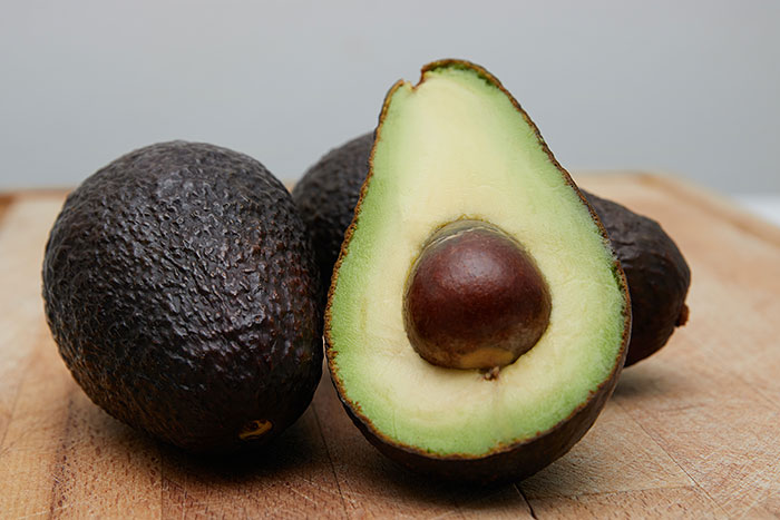 Food history facts: Whole and halved avocado revealing its seed on a wooden cutting board, highlighting the story behind what we eat.