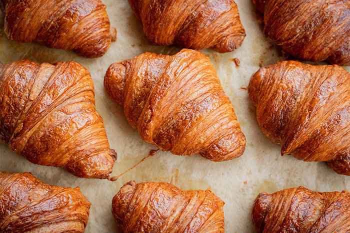 Rows of golden-brown croissants on parchment paper, illustrating delicious food history facts.