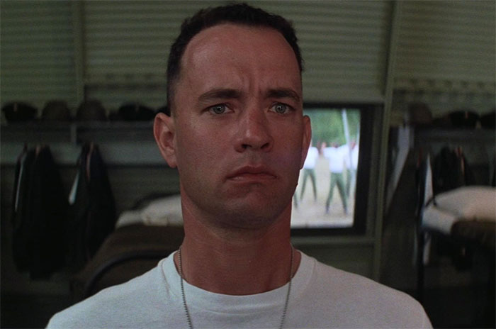 Forrest Gump wearing a white t-shirt looking thoughtful in a military barracks scene for Forrest Gump quotes.