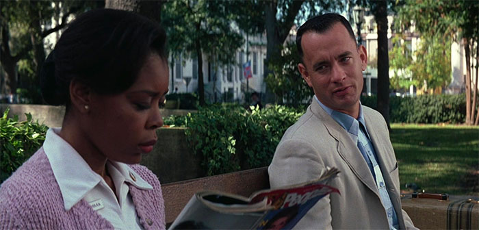 Forrest Gump talking with a woman on a bench in a park, capturing a memorable moment from Forrest Gump quotes.