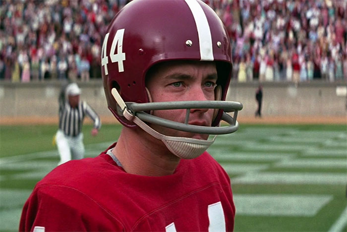 Forrest Gump playing football on the field wearing a red helmet and jersey in a scene from Forrest Gump quotes collection