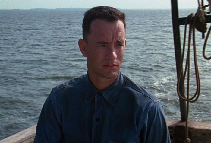 Forrest Gump in a blue shirt on a boat with ocean background, representing iconic Forrest Gump quotes scene.