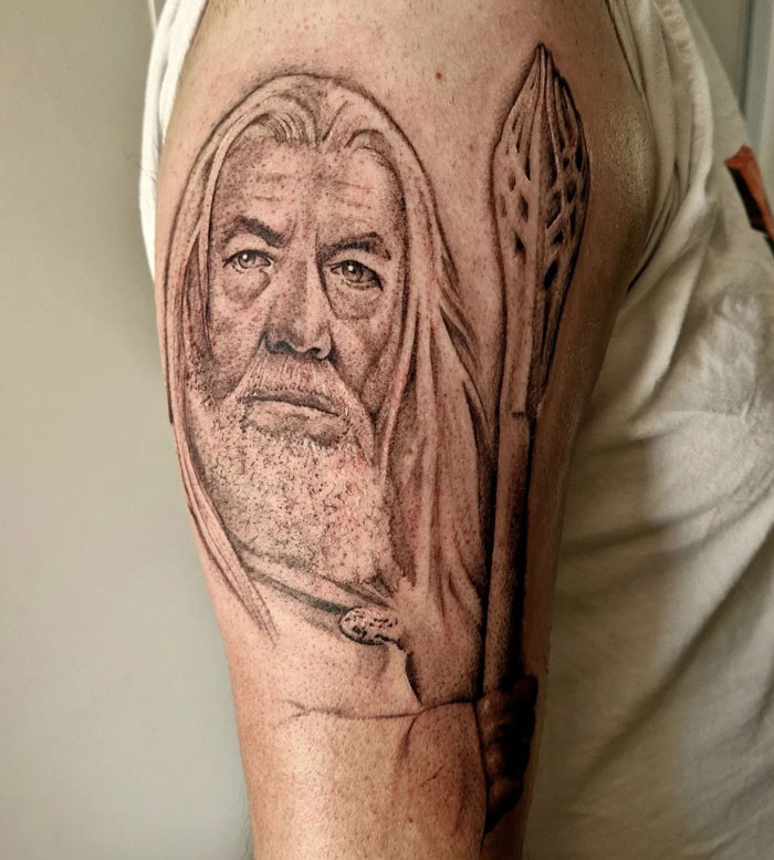 Lord of the Rings tattoo depicting a wizard holding a staff on an upper arm.