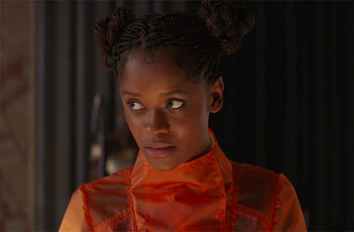 Shuri in orange outfit looking sideways