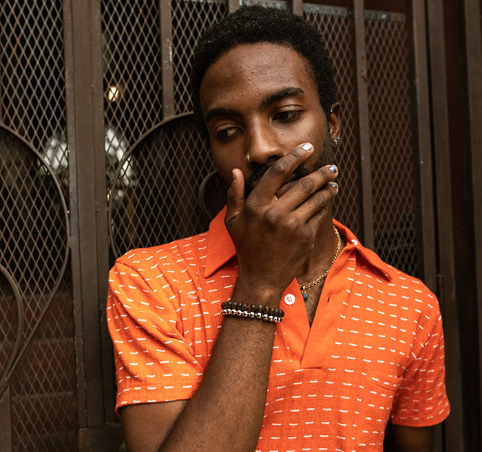 Young man in an orange shirt looking embarrassed and covering his mouth, reflecting on embarrassing things told to impress others