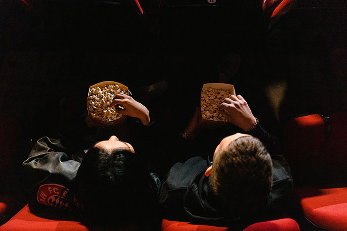 Two people eating popcorn in a dark movie theater, capturing an embarrassing moment shared by internet users to impress others.