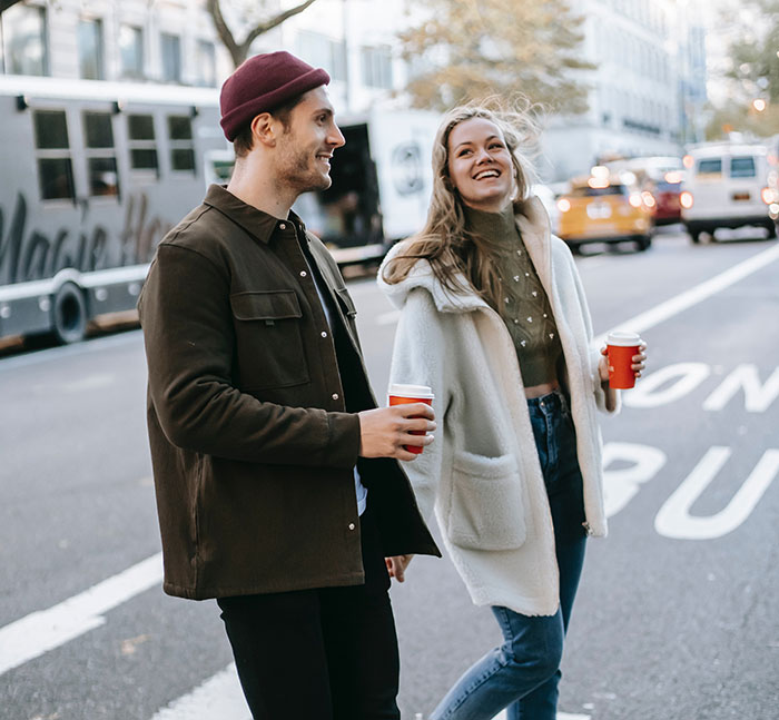Two people holding coffee cups and smiling on a city street, illustrating embarrassing things people told to impress online.