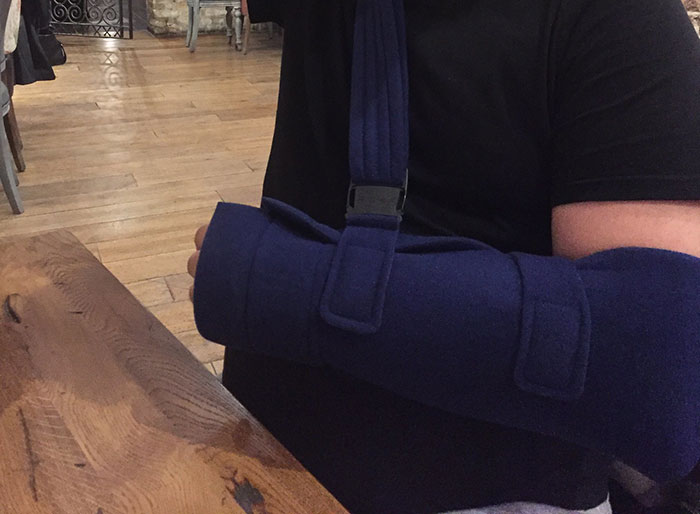 Person wearing a dark blue arm brace sitting at a wooden table, illustrating embarrassing stories to impress others.