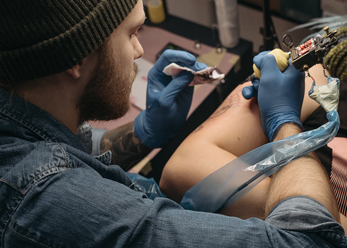 Tattoo artist in blue gloves working on a person's arm tattoo, highlighting a key issue in mother-daughter relationships. Tattoo artist in blue gloves working on a person's arm tattoo, highlighting a key issue in mother-daughter relationships.