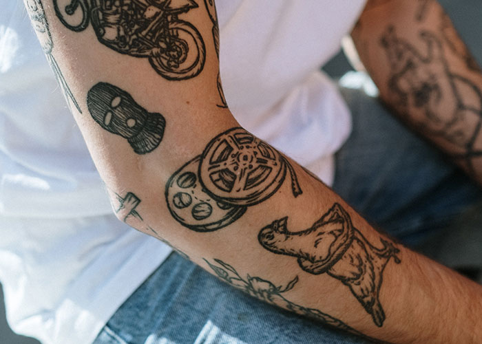 Close-up of a person's arm featuring several tattoos, including a film reel and a motorcycle. Close-up of a person's arm featuring several tattoos, including a film reel and a motorcycle.