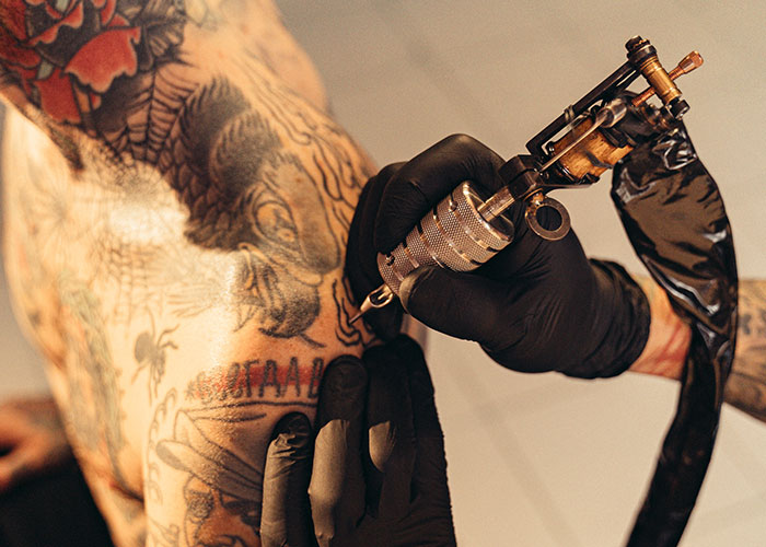 Tattoo artist using a machine to ink a person's arm in a studio setting. Tattoo artist using a machine to ink a person's arm in a studio setting.