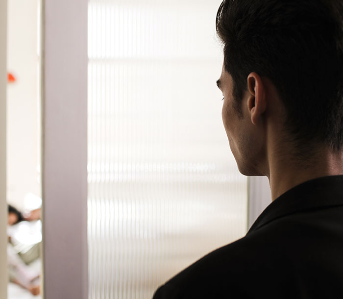 Man in black jacket looking through a frosted glass door, portraying the discovery of disturbing secrets about someone close.