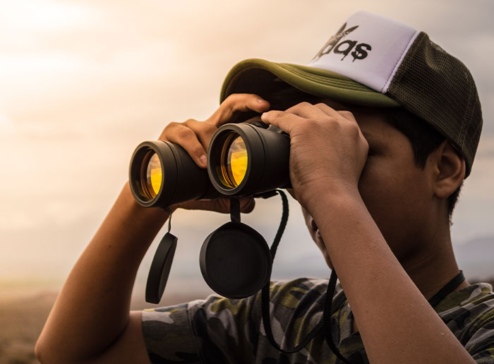 Young man in a cap looking through binoculars, symbolizing uncovering disturbing secrets about someone close to him.