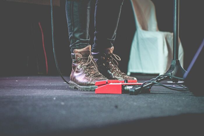 Close-up of worn leather boots on stage floor with cables and pedals, illustrating things people have learned never to buy cheap.