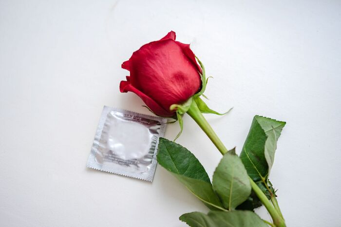 Red rose next to a silver c****m wrapper on a white surface, illustrating things people have learned never to buy cheap.