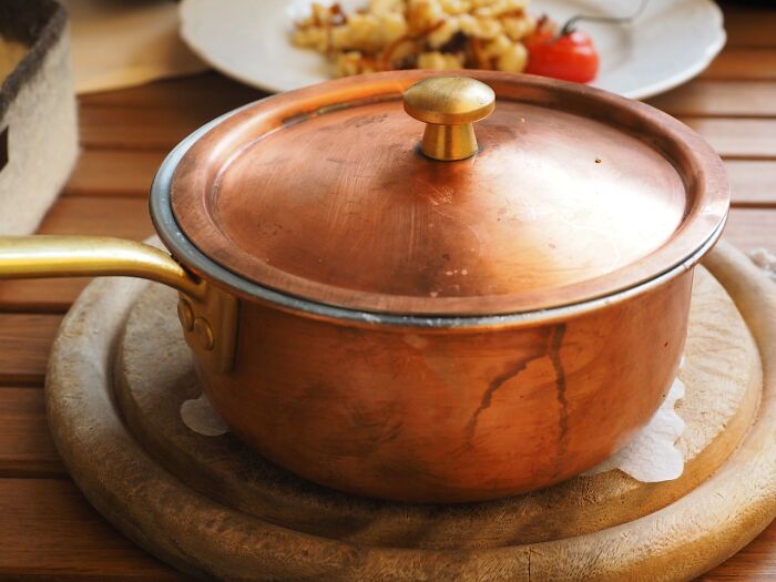 Copper cooking pot with lid on wooden trivet, illustrating things people have learned never to buy cheap.