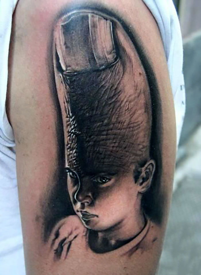 Tattoo on arm featuring a child's face with a finger replacing the top of their head, creating an unusual design.